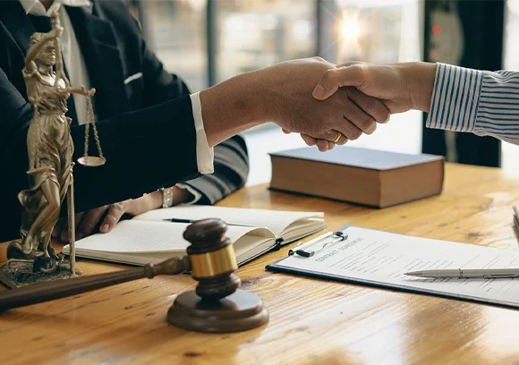 Two hands shaking above a stack of documents, representing agreement and professionalism in legal services.