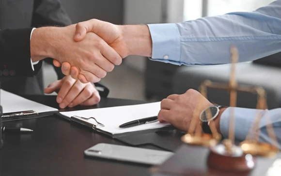 Close-up of two individuals shaking hands over legal documents, symbolizing the agreement and professional relationship in securing fast bail bonds.
