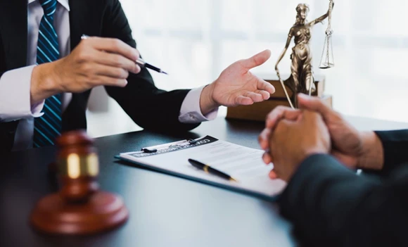 Two professionals engaging in a conversation over legal documents on a table, with a gavel and scales of justice in the background, emphasizing collaboration in bail bond services.